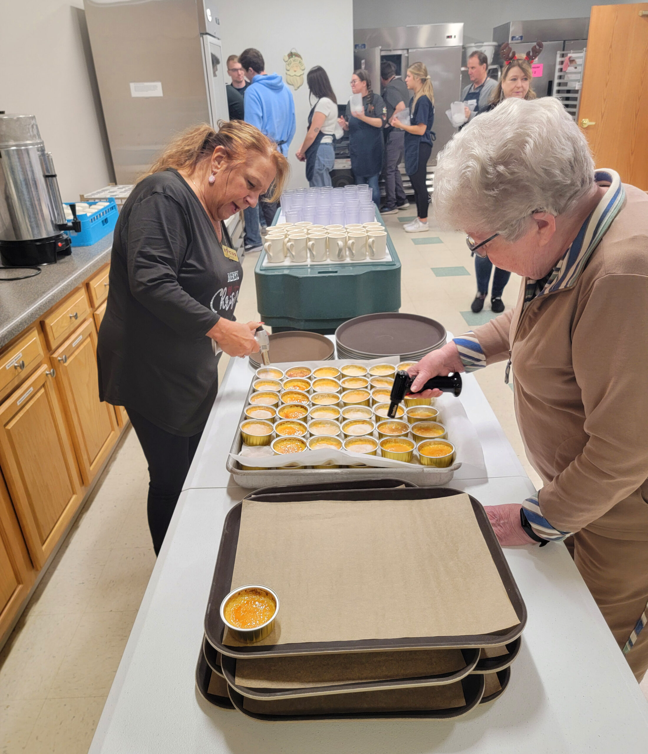 21st Anniversary Meal - Volunteers here torch the sugar atop the Creme Brulee for dessert while others wait in line to fill their water pitchers for the tables.